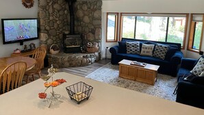 A cozy living room with a stone wall, a fireplace, a television, a sofa, and a dining area.