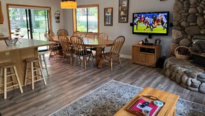 A dining area with a wooden table and chairs, a TV mounted on the wall, and a stone fireplace.