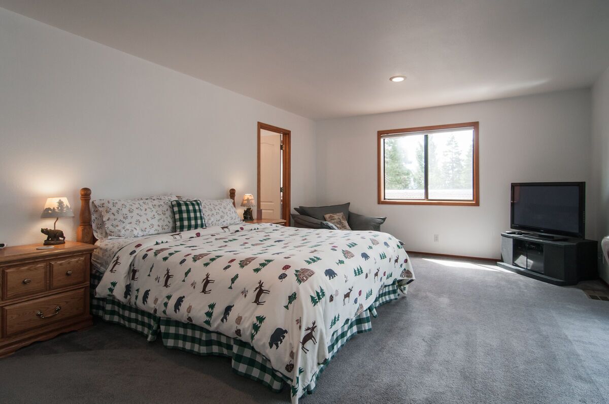 A bedroom with a bed, a nightstand, a dresser, a TV, and a window.