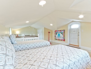 A bedroom with two beds, a large window, a door, and a painting on the wall.