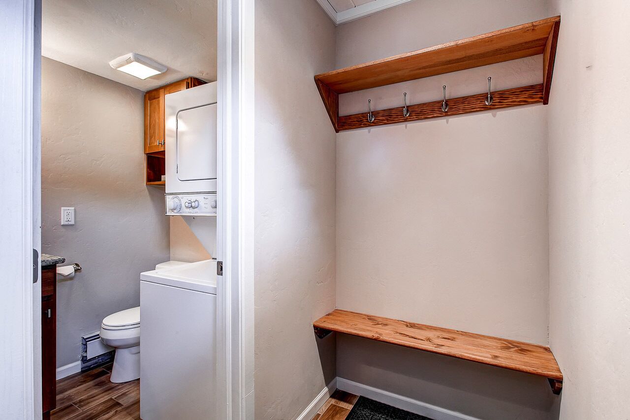 A small bathroom with a toilet, a white sink, and a wooden shelf above the toilet.