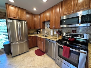 A modern kitchen with wooden cabinets, stainless steel appliances, granite countertops, and a red rug.