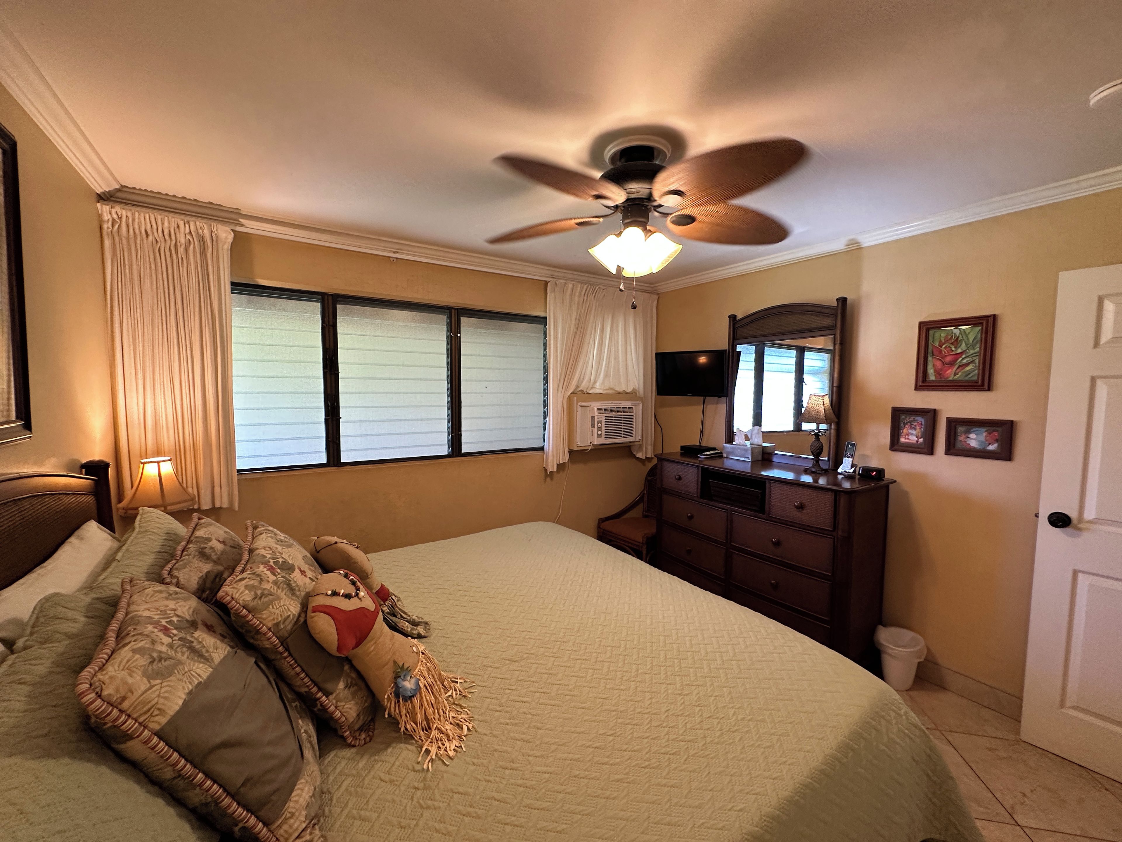 A bedroom with a bed, a ceiling fan, a dresser, a TV, and a window with curtains.