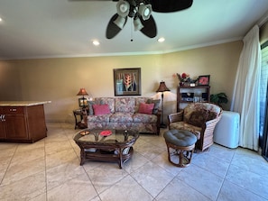 A living room with a sofa, armchair, coffee table, and a ceiling fan.