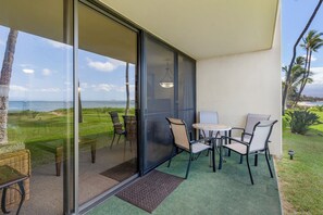 A balcony with a glass door, outdoor seating, and a view of the ocean.