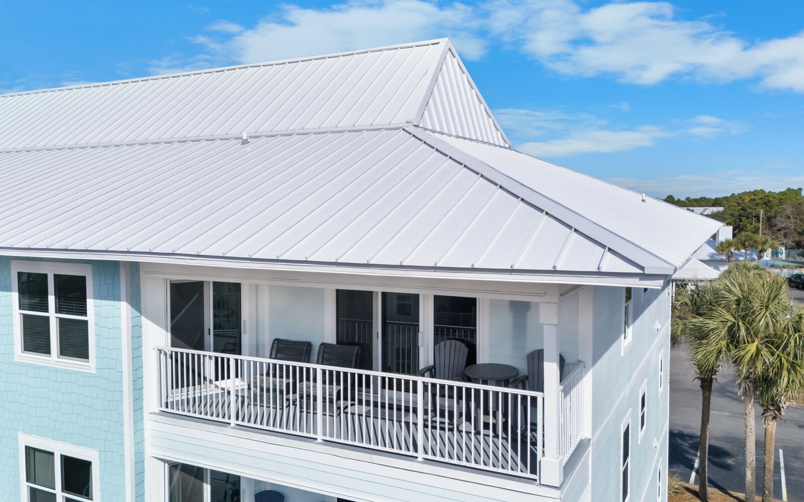 Modern coastal property featuring white metal roofing and covered balcony with scenic neighborhood views.