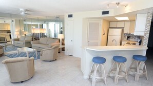 Una cocina moderna con una isla central, taburetes de bar y una zona de comedor con sofá y sillas.