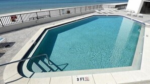 Piscina con indicador de profundidad de 3 pies, rodeada de sillas de descanso y barandilla, con vistas al océano.