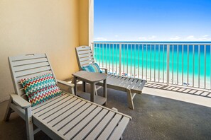 A balcony with a view of the beach, a chair with a patterned pillow, and a small table. - Ultimate Beachfront Getaway: Gulf front condo on the 12th floor! (Panama City Beach)