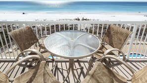 Mesa redonda de cristal con sillas de mimbre en un balcón con vista a una playa.