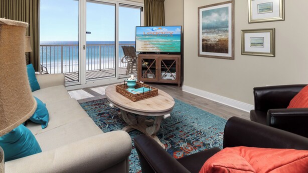 Una sala de estar con vista al océano, un televisor mostrando 'Legacy Vacations' y un comedor con una mesa y sillas.