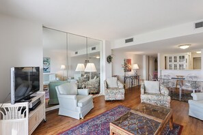 A spacious living room with a television, two armchairs, a sofa, a coffee table, and a dining area with chairs and a table.