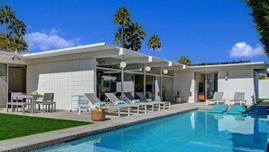 Un espace piscine moderne, doté de chaises longues et d’un coin repas.