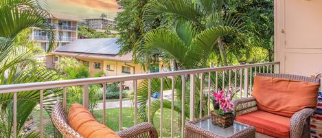 A balcony with wicker furniture, a glass table, and a view of surrounding buildings and greenery.