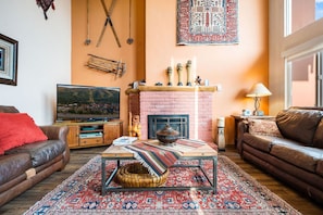 A cozy living room with a brick fireplace, a television, and a comfortable sofa.