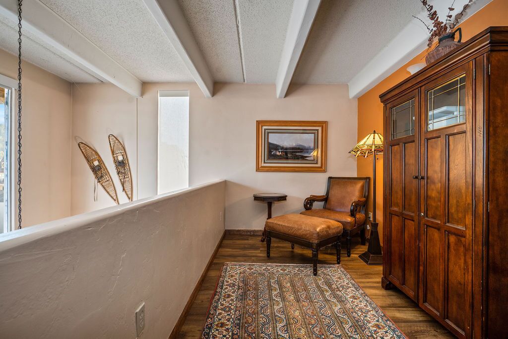 A room with a patterned rug, a wooden cabinet, a chair, and a framed picture on the wall.