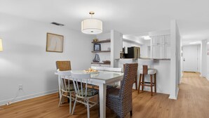 Una cocina moderna con armarios blancos, una zona de comedor con mesa de vidrio y sillas de mimbre.