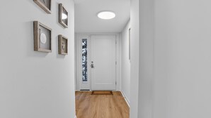 Un pasillo con piso de madera, paredes blancas y una puerta blanca con un panel de vidrio.