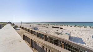 Uitzicht op een strand vanaf een houten looppad, met een zandstrand en een heldere lucht.