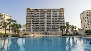 Een hotel met een groot zwembad, meerdere balkons en palmbomen.