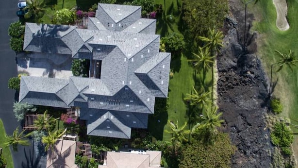 A large, multi-story house with a complex roof structure, surrounded by lush greenery and a golf course. - Summer Special! Discover luxury at Leilani Kai, a 3BR condo in beautiful Waikoloa, HI. (Waikoloa Village)
