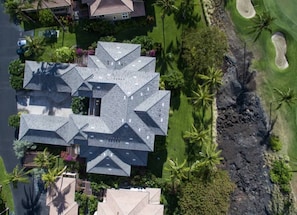 Een groot, meerlaags huis met een ingewikkeld dak, omgeven door weelderige begroeiing en een golfbaan.