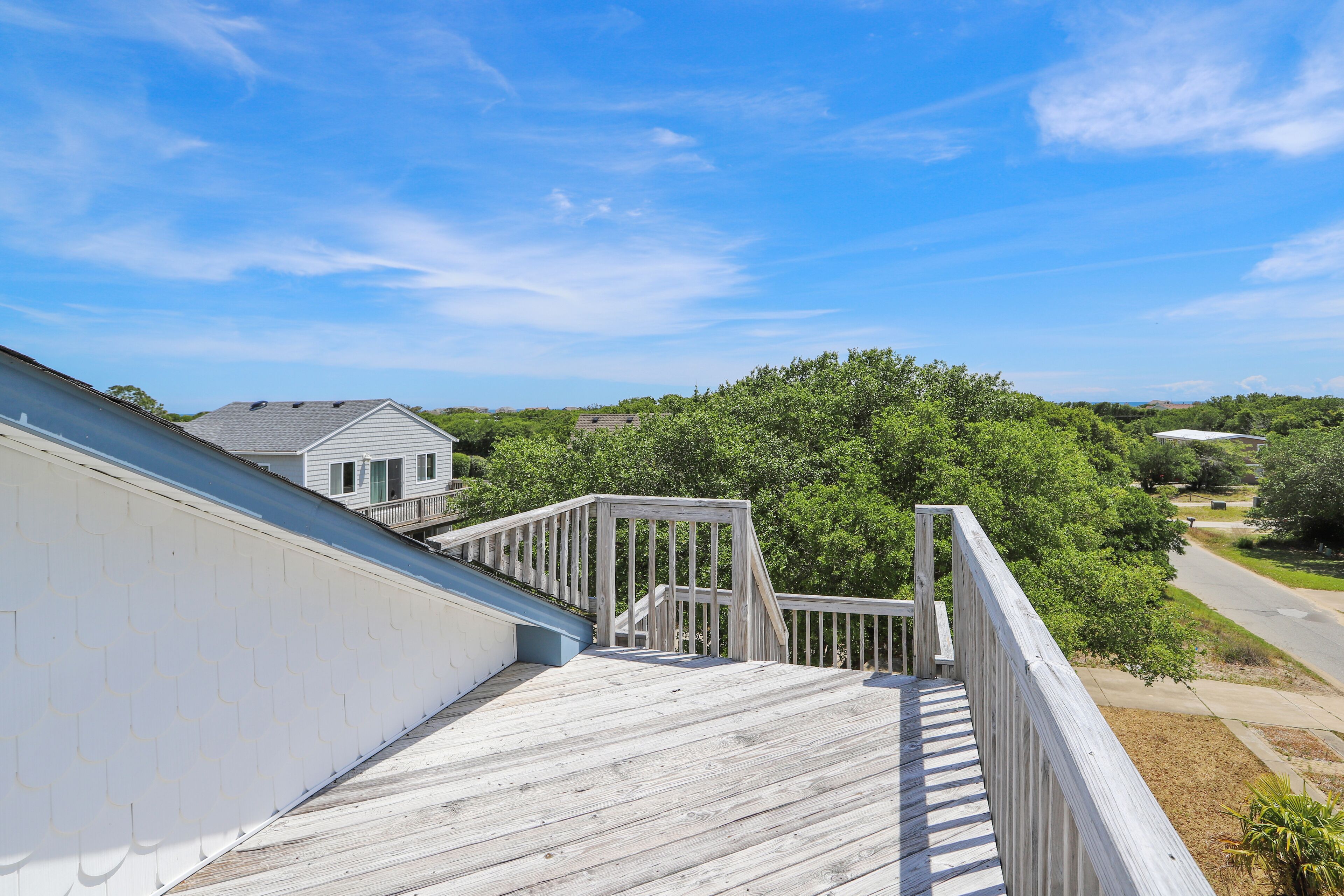 A wooden deck with a railing, overlooking a residential area with houses and trees.