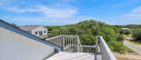 A wooden deck with a railing, overlooking a residential area with houses and trees.