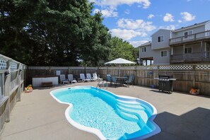 Un jardin avec une piscine, des chaises longues, un barbecue et une clôture en bois.