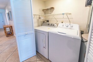 A laundry area with two stacked washers and dryers, a drying rack, and a small wooden stool.