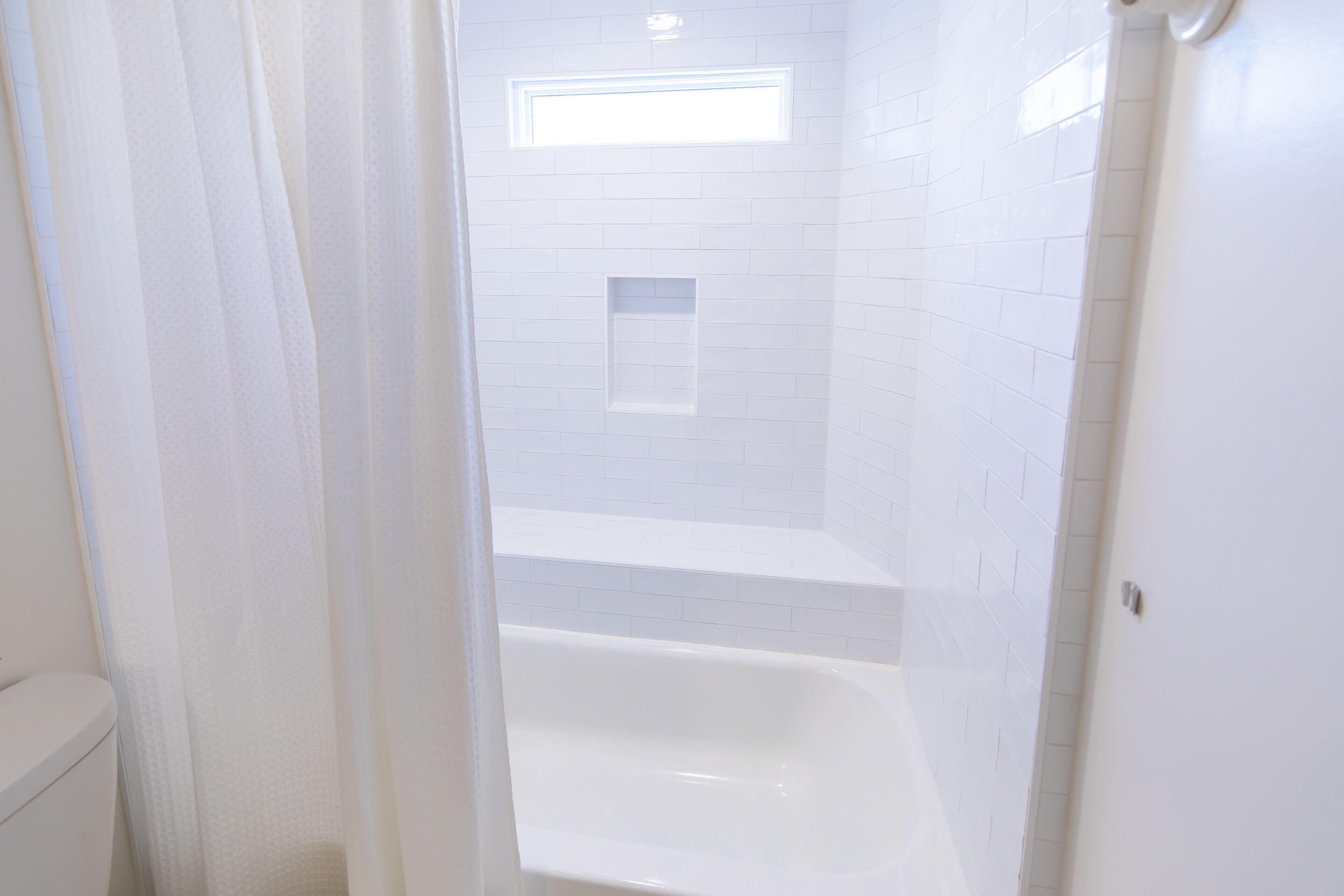 Une salle de bain blanche avec une baignoire, un espace douche et une petite fenêtre.