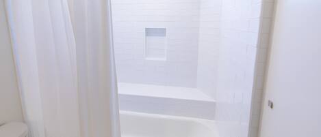 Une salle de bain blanche avec une baignoire, un espace douche et une petite fenêtre.