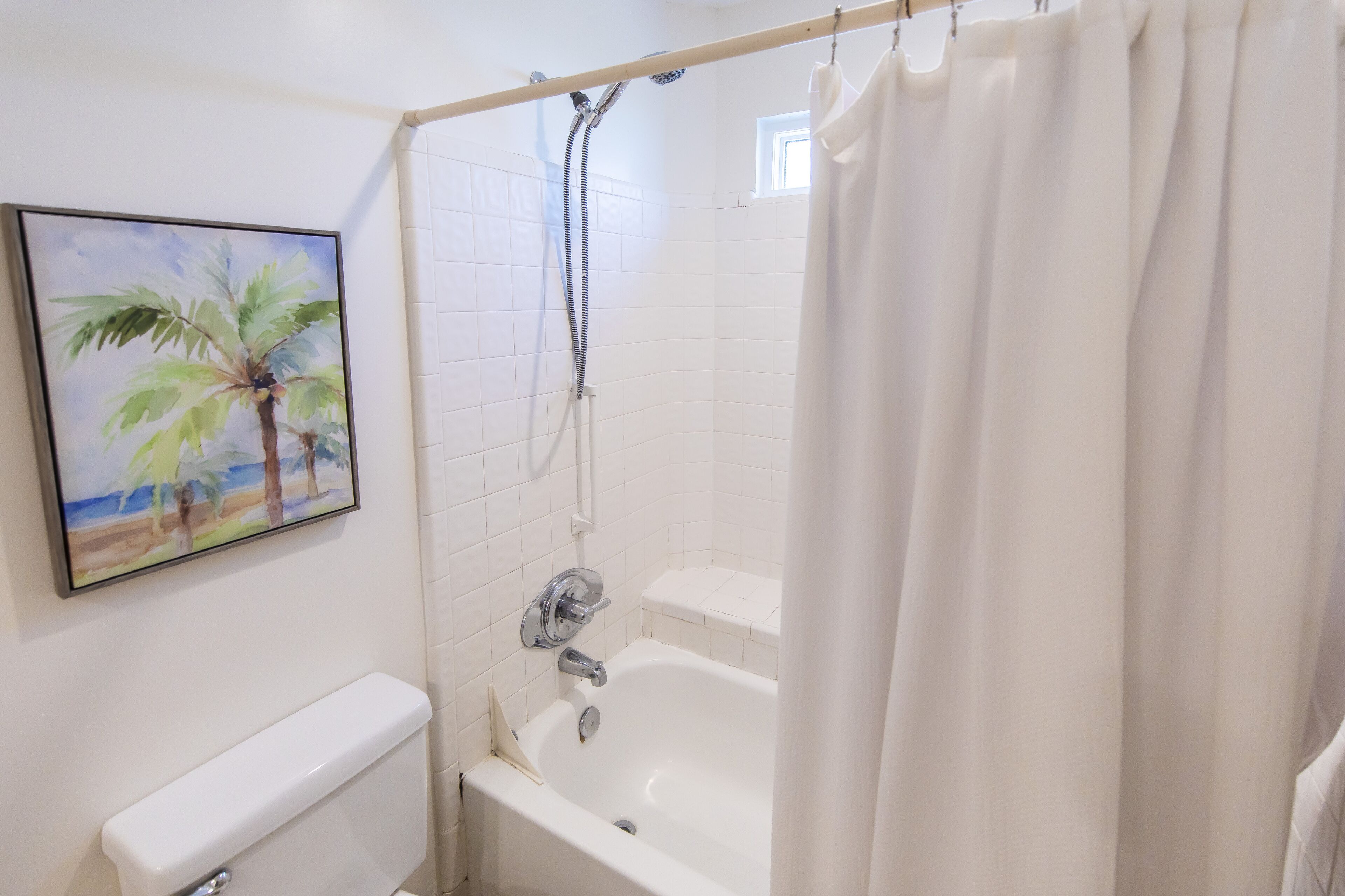 Ein Badezimmer mit Badewanne, Toilette, Dusche mit Duschvorhang und einem Palmenbild.
