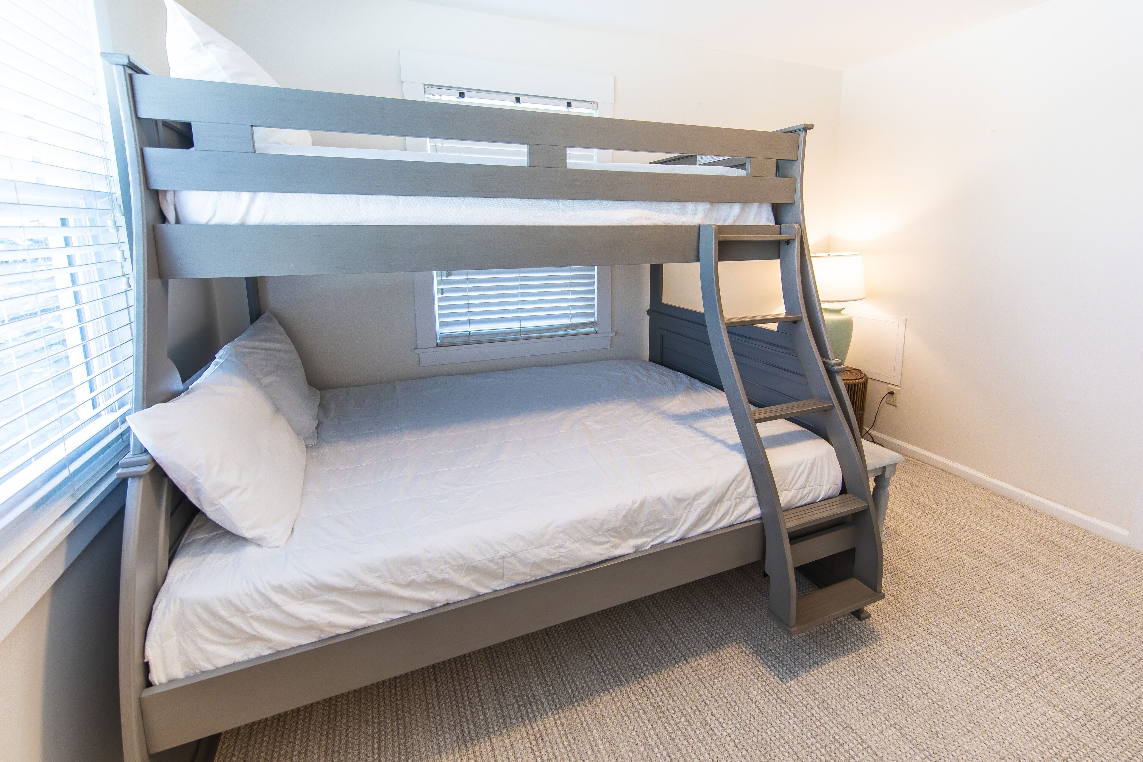 A bunk bed with a window, a bedside table, and a lamp.