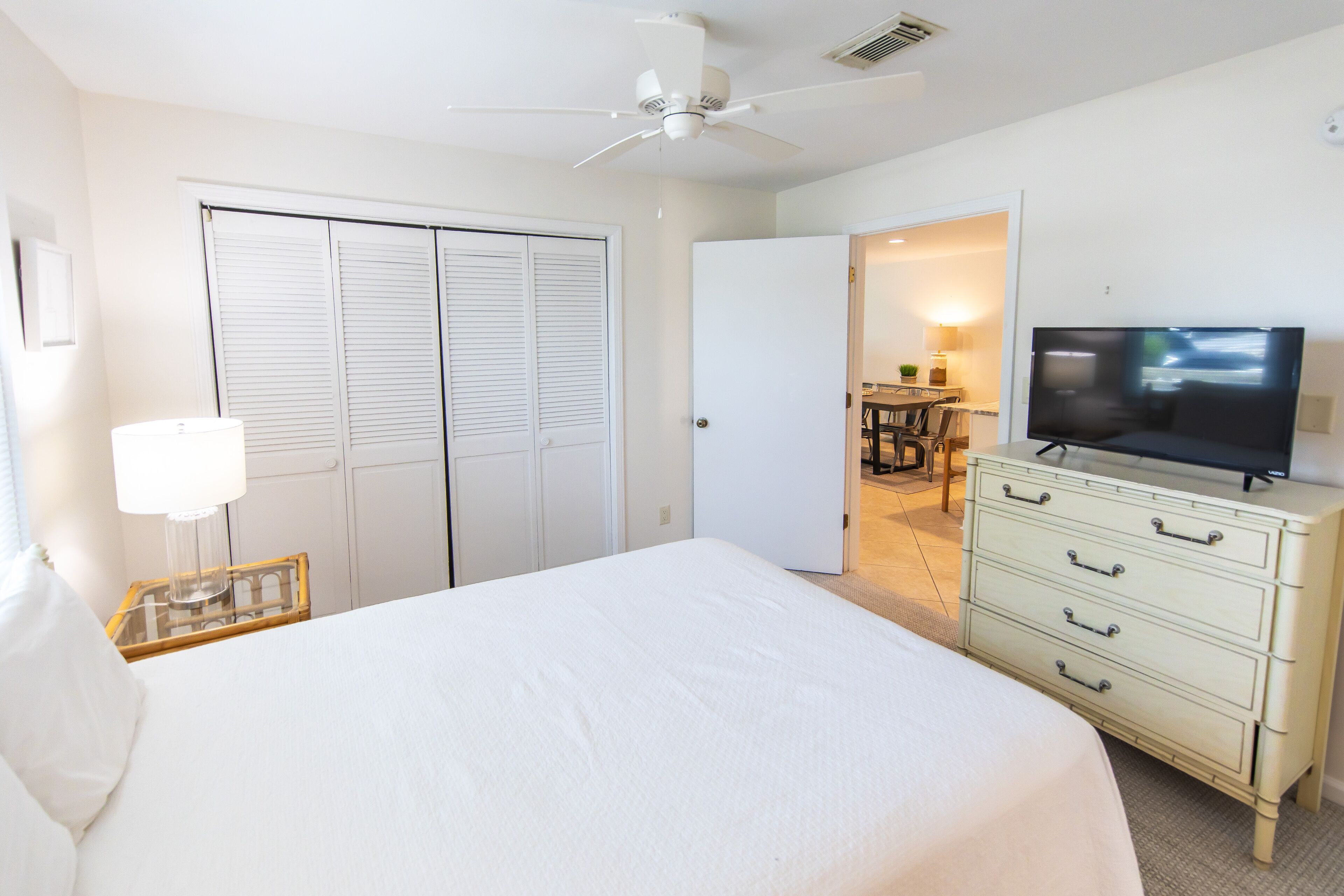 A hotel room with a bed, a television, a dresser, and a ceiling fan.