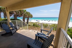 A covered outdoor area with Adirondack chairs, a view of a beach, and a clear sky.