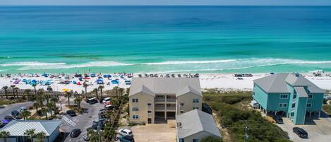 A beachfront hotel with a parking lot, beach umbrellas, and a view of the ocean.