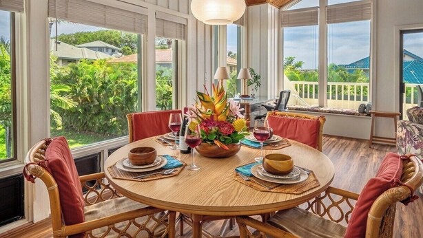 A round dining table with chairs, a flower centerpiece, and wine glasses. - Manualoha 1105 Ocean Mountain views By Suite Paradise (Koloa)