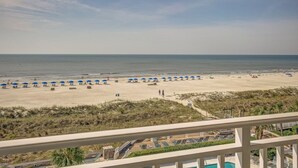 Een strand met blauwe parasols en ligbedden, een zwembad en uitzicht op de oceaan.