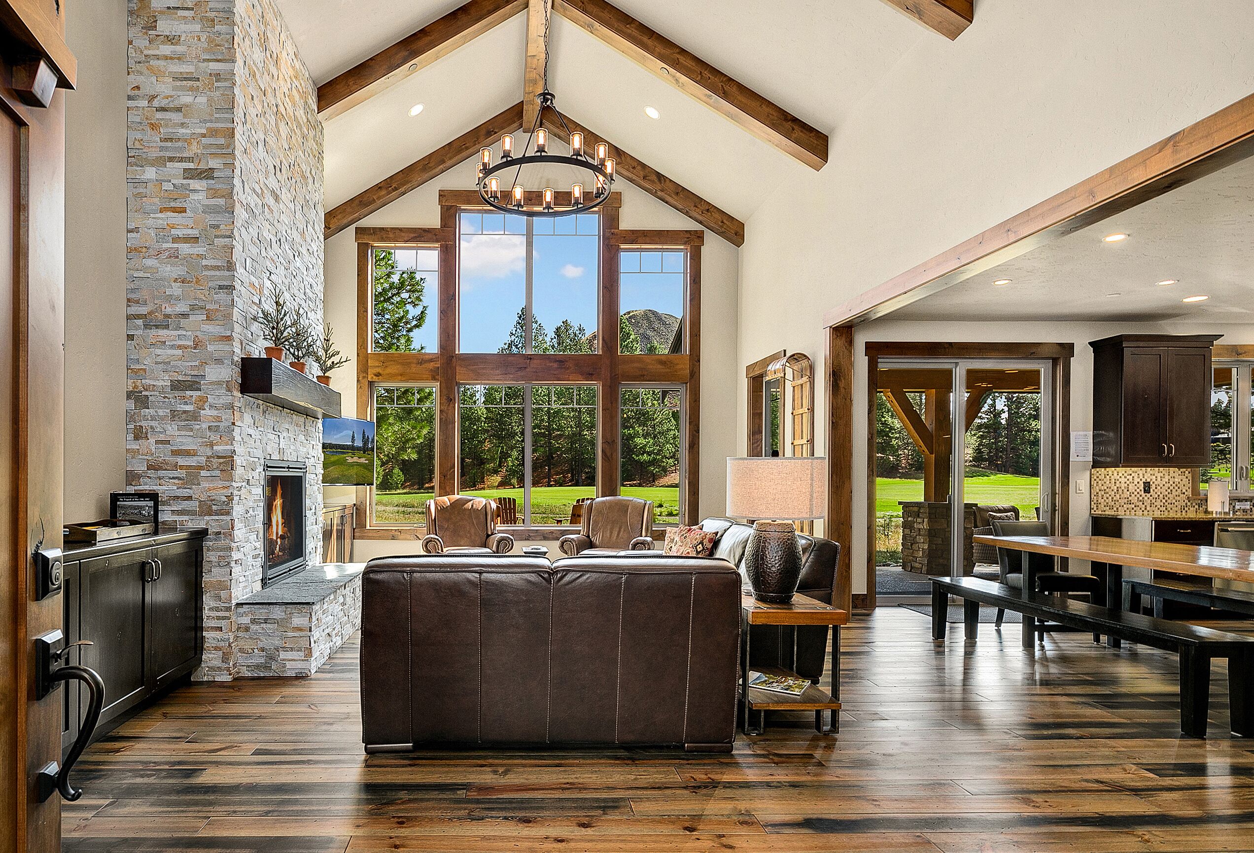 A spacious living room with a stone fireplace, large windows, and a high ceiling with exposed beams. - Brand New Golf Course Stunner! Short Walk to the Winery * Hot Tub * Fire Pit (Cle Elum)