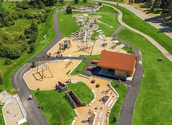An aerial view of a park with a playground, a building with a red roof, and winding roads.