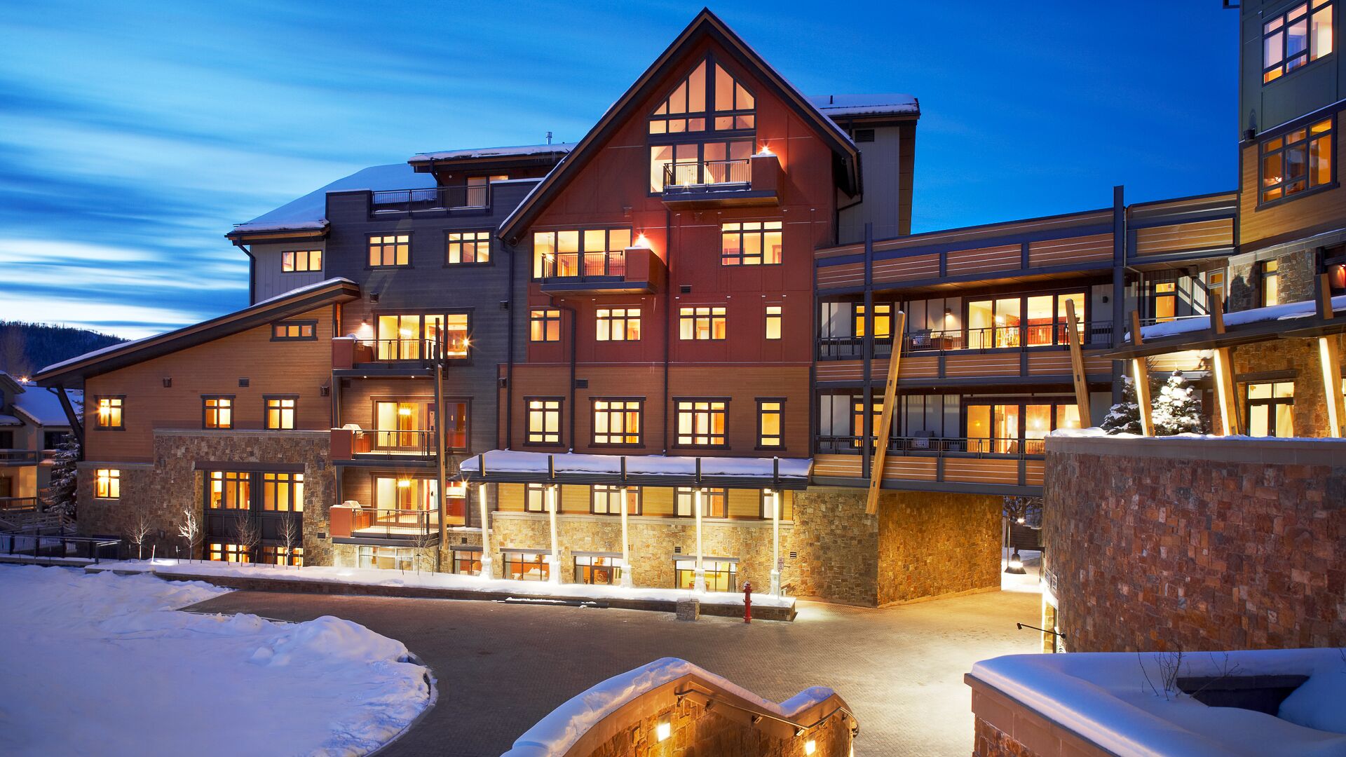A multi-story hotel with a ski resort exterior, featuring balconies, large windows, and a stone facade.