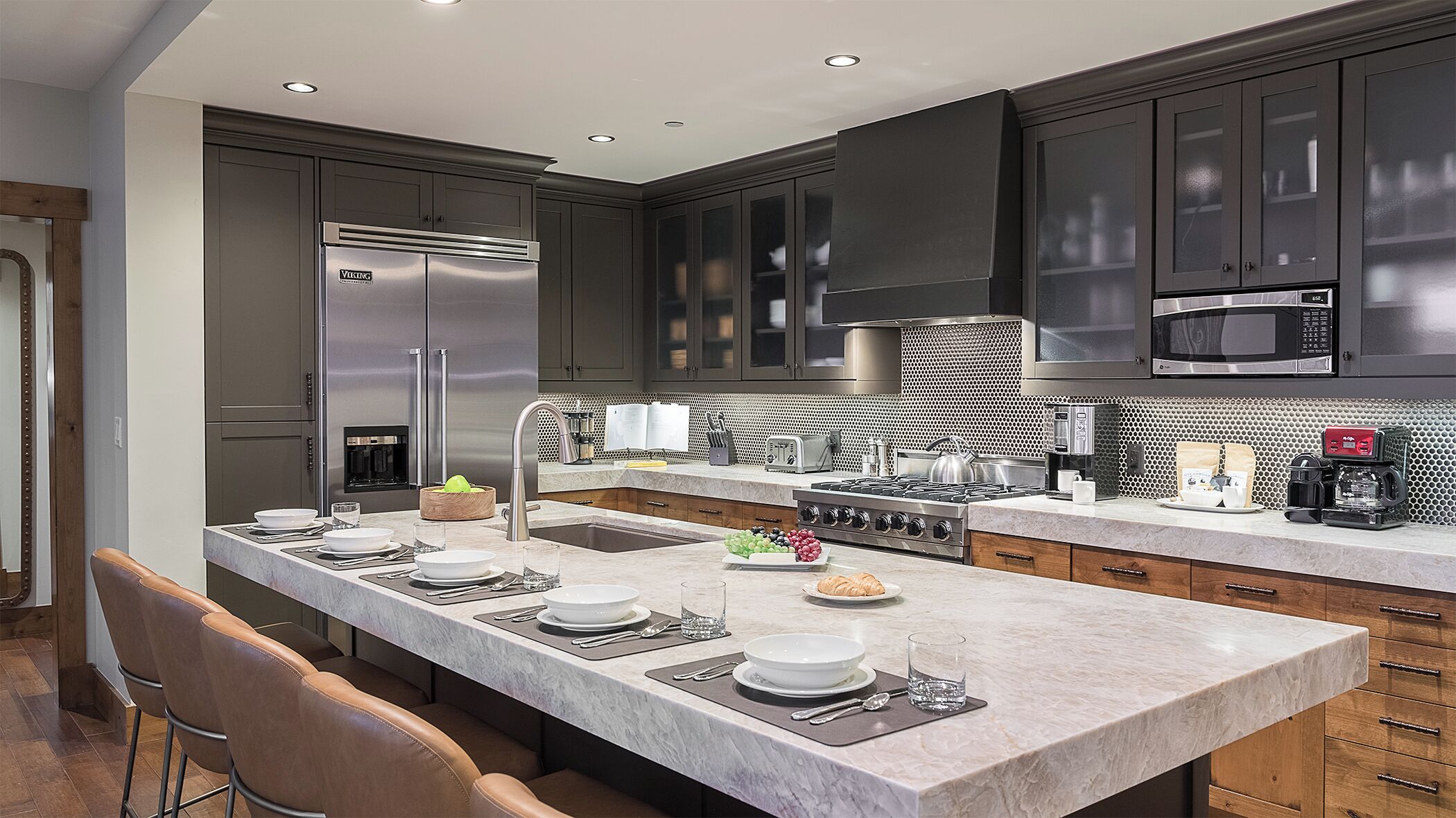 A modern kitchen with dark cabinetry, stainless steel appliances, a large island with seating, and a tiled backsplash.