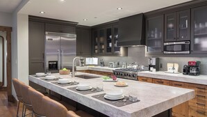Een moderne keuken met donkere kastjes, roestvrijstalen apparatuur, een groot eiland met zitplaatsen en een betegelde achterwand.