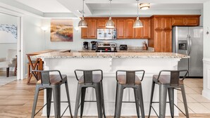 Una cocina moderna con armarios de madera, una isla grande, electrodomésticos de acero inoxidable y taburetes de bar.