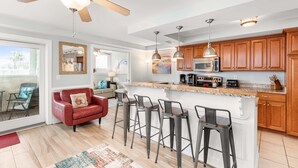 Una cocina moderna con una isla central, taburetes de bar, armarios de madera y un ventilador de techo.
