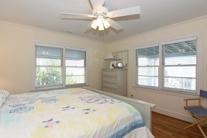 A bedroom with a bed, dresser, chair, and ceiling fan.