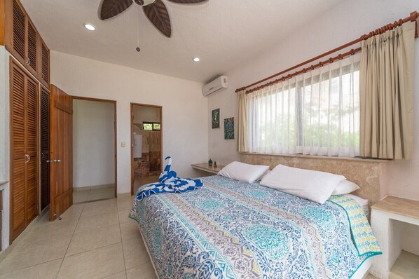 A bedroom with a bed, a ceiling fan, a window with curtains, and a wooden wardrobe.
