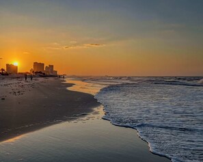 Ein Strand mit Sonnenuntergang, Meereswellen und Gebäuden im Hintergrund.