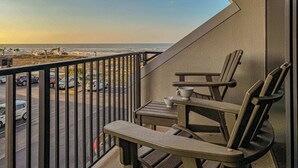Een balkon met uitzicht op het strand en geparkeerde auto's.